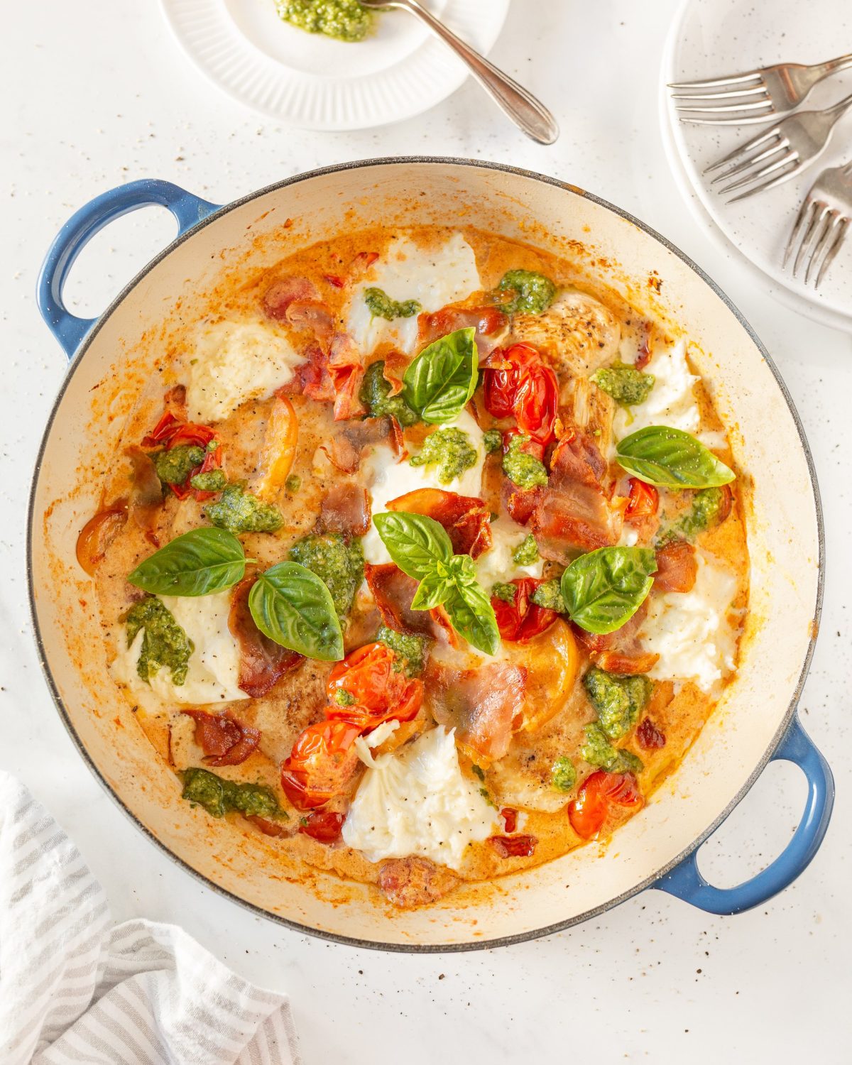 Caprese Peach and Pesto Chicken cooked in a skillet and garnished with fresh basil leaves.