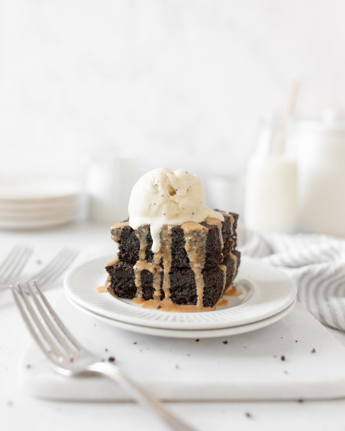 2 Flourless Peanut Butter Brownies stacked on two small plates and topped with vanilla ice cream.