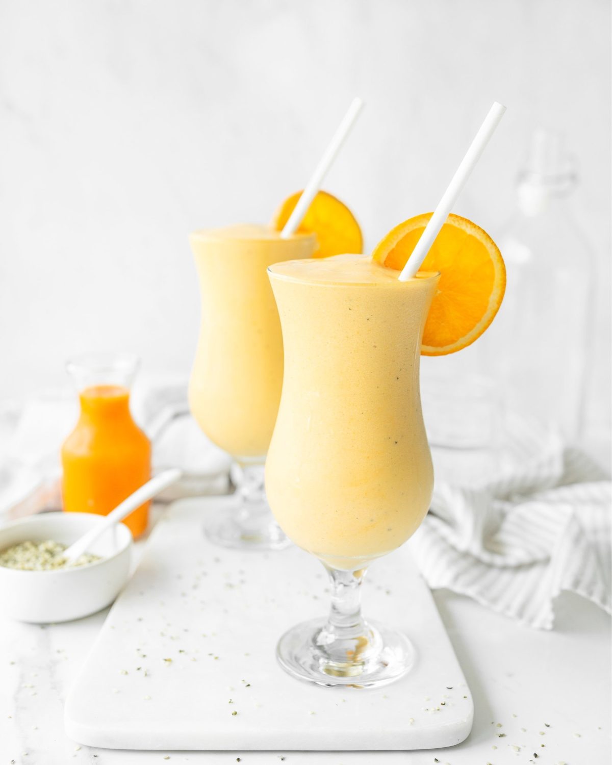 Turmeric smoothies portioned into glasses and garnished with an orange slice and a straw.