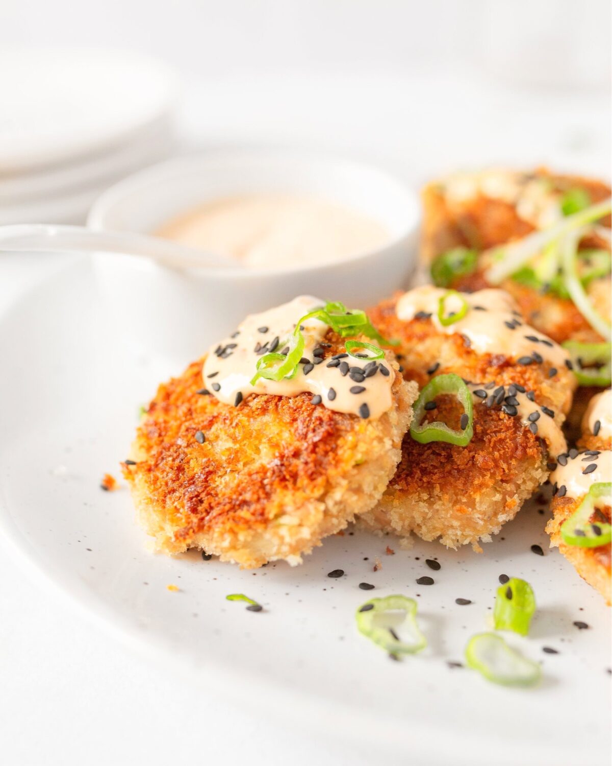 Asian-style tuna cakes plated and topped with spicy mayo, green onions and black sesame seeds.
