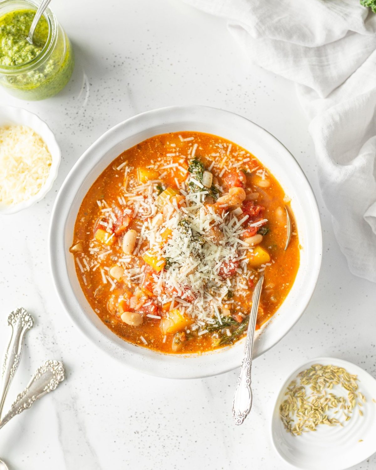 White Bean Minestrone Soup in a bowl with a spoon, garnished with fresh grated parmigiana.