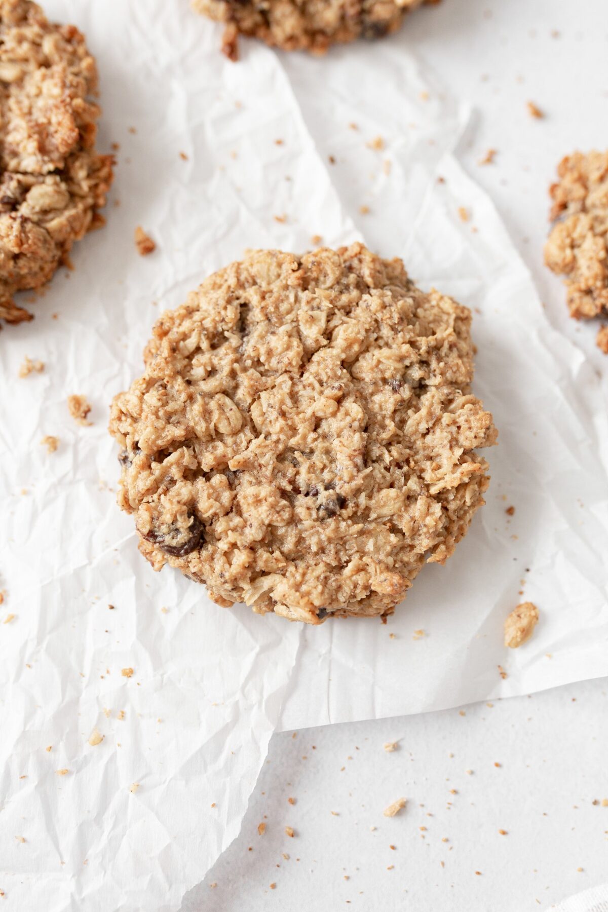 A Flourless Coconut Oatmeal Cookie on parchment paper with crumbs around it.