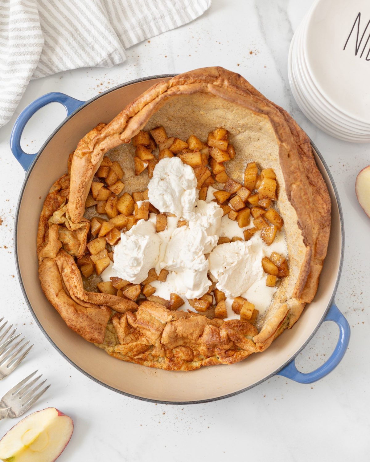 Gluten-free Apple Cinnamon Dutch Baby baked in a pan and topped with sautéed apples and whipped cream.