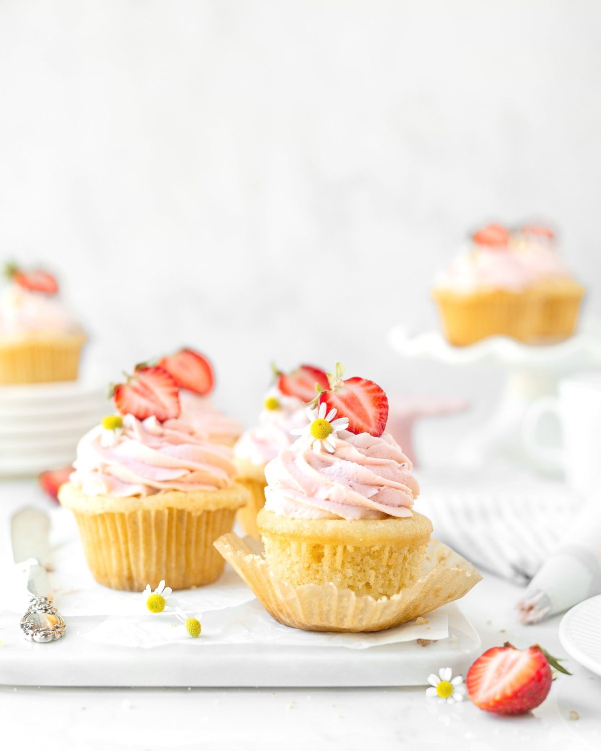 Gluten Free Strawberries and Cream Cupcakes styled on a marble board and topped with camomile flowers.