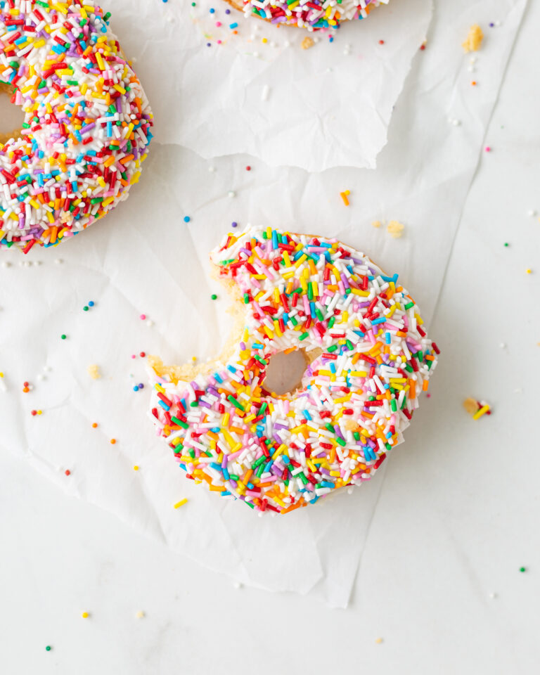 Gluten Free Donuts on parchment paper. One has a bite taken out of it.