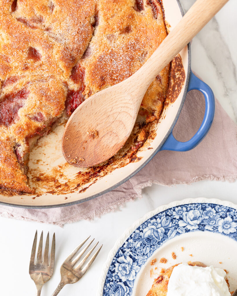 Gluten Free Strawberry Rhubarb Spoon Cake baked until lightly golden and a small amount scooped out with a spoon onto a small dessert plate. It's topped with whipped cream. 