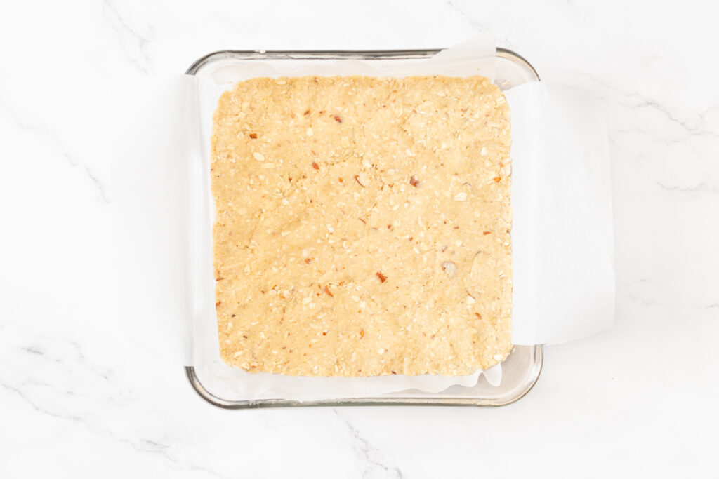 Process shot #3: 1/2 - 2/3 of the oat crumble mixture pressed into the bottom of a prepared 8" x 8" pan.