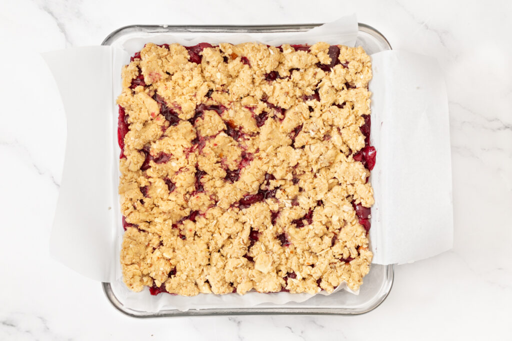 Process shot #4: cherry compote and oat crumble topping layered on top of the crust in the prepared pan.