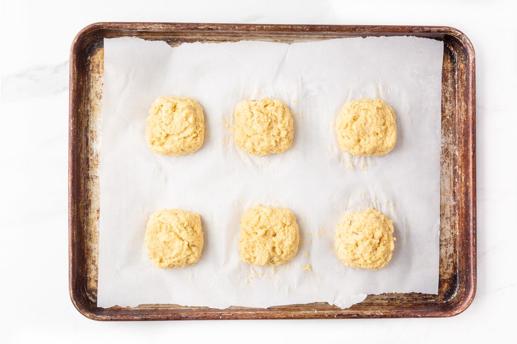 Process shot #4: biscuit dough scooped onto a parchment lined baking sheet in 6 equal mounds. 