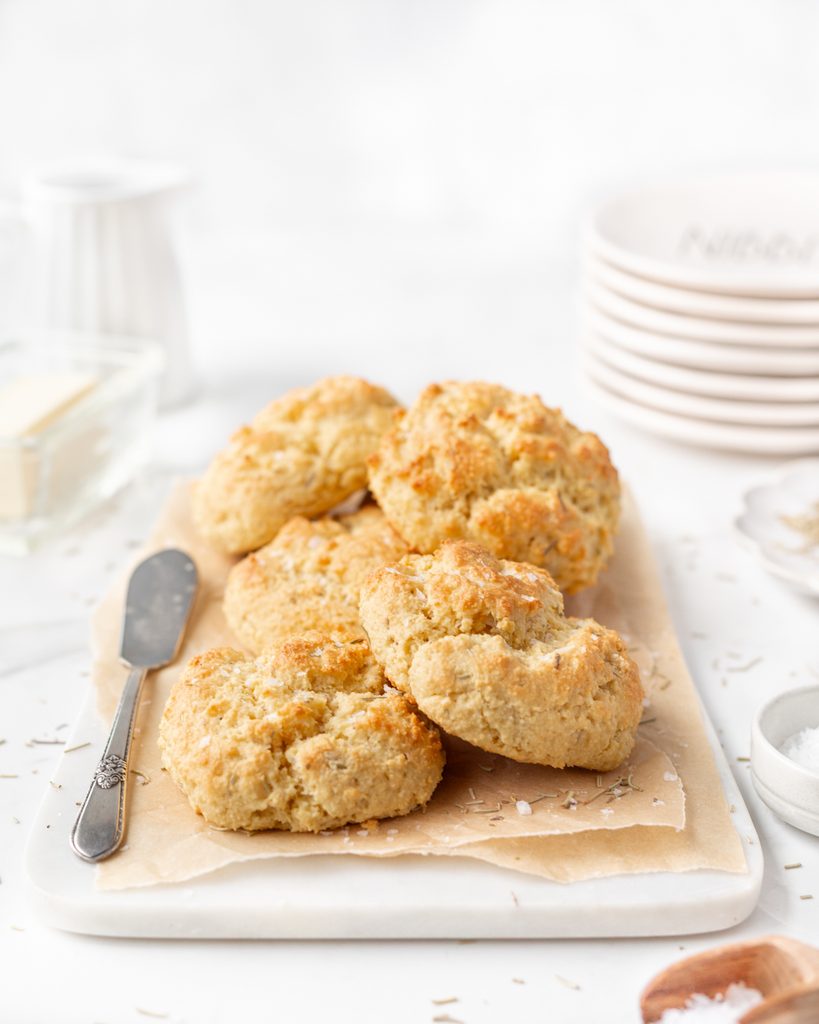 Almond Flour Biscuits with Rosemary  placed on top of a parchment-lined marble serving board and sprinkled with flakey sea salt. 