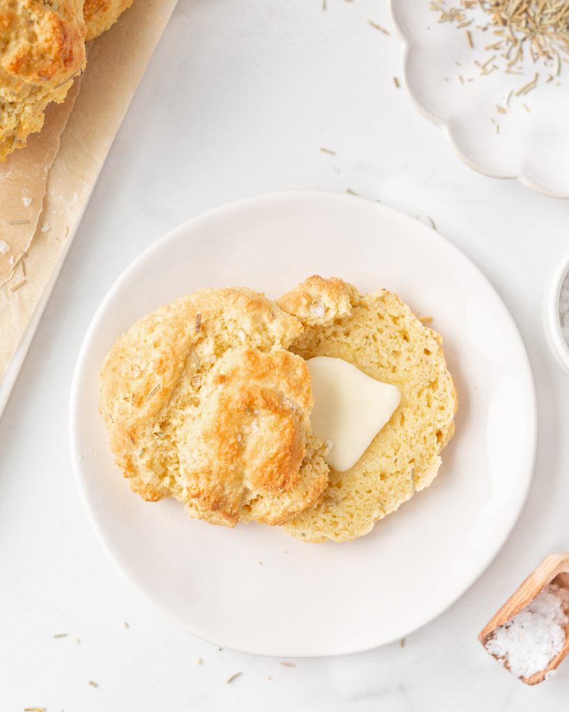 A Rosemary Almond Flour Biscuit cut open on a small plate with butter on top.