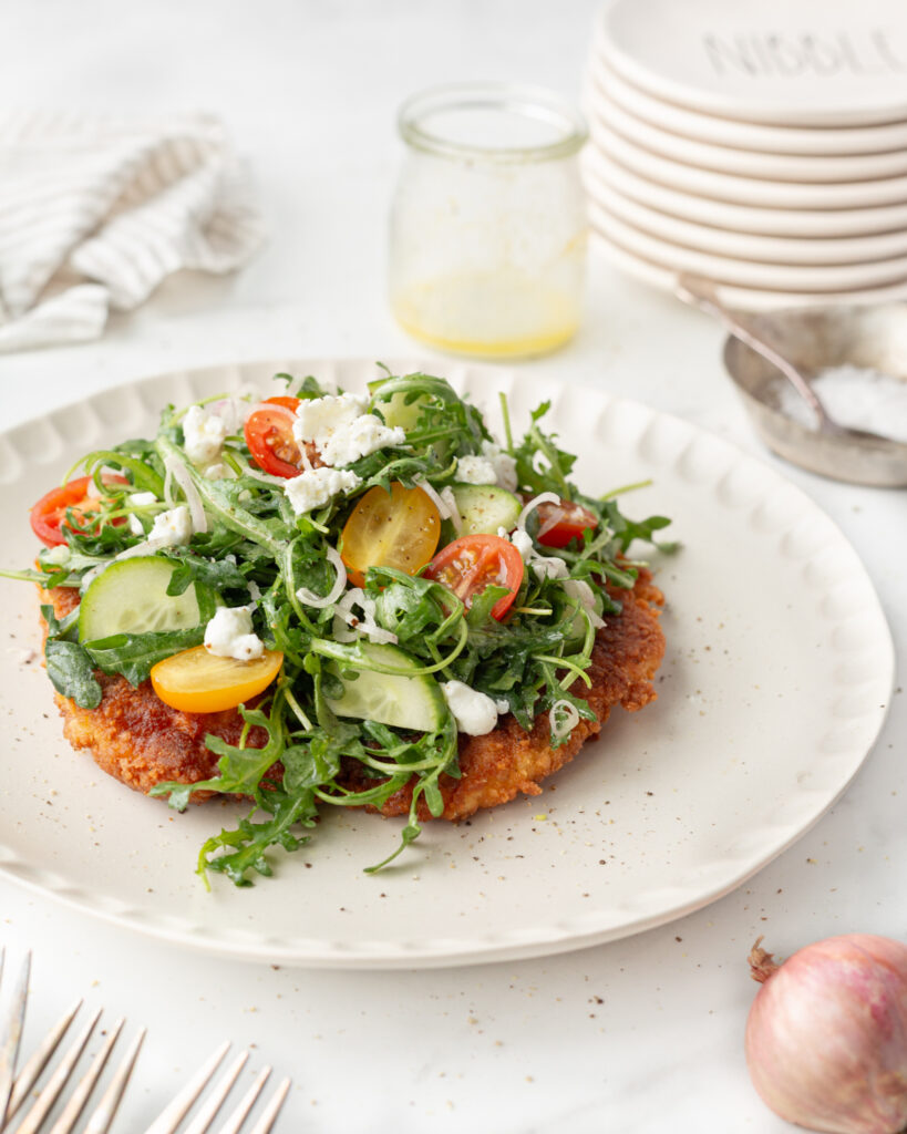 Crispy Chicken and Rocket Salad plated and topped with creamy goat cheese. 