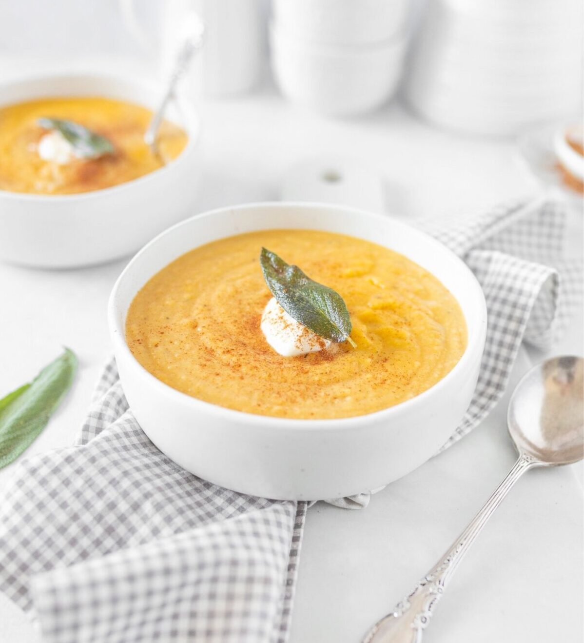 Gluten Free Roasted Butternut Squash and Apple Soup served in a bowl and topped with a dollop of greek yogurt and a crispy sage leaf.
