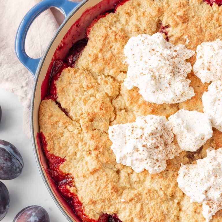 Gluten Free Prune Plum Cobbler baked in a skillet and topped with dollops of whipped cream.