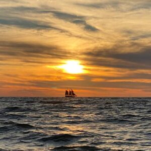A peaceful ocean scene at sunset featuring a Pirate ship silhouetted against a colorful sky. Sunshine City Massage and Spa