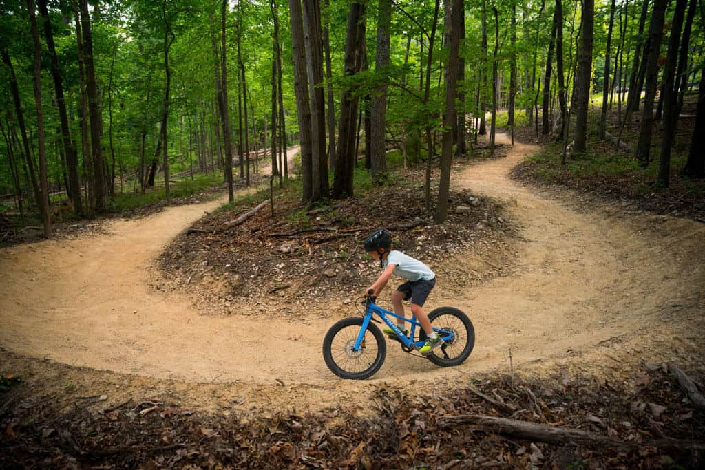 Young rider in a helmet carving a smooth, banked turn on a Sunset Park singletrack trail