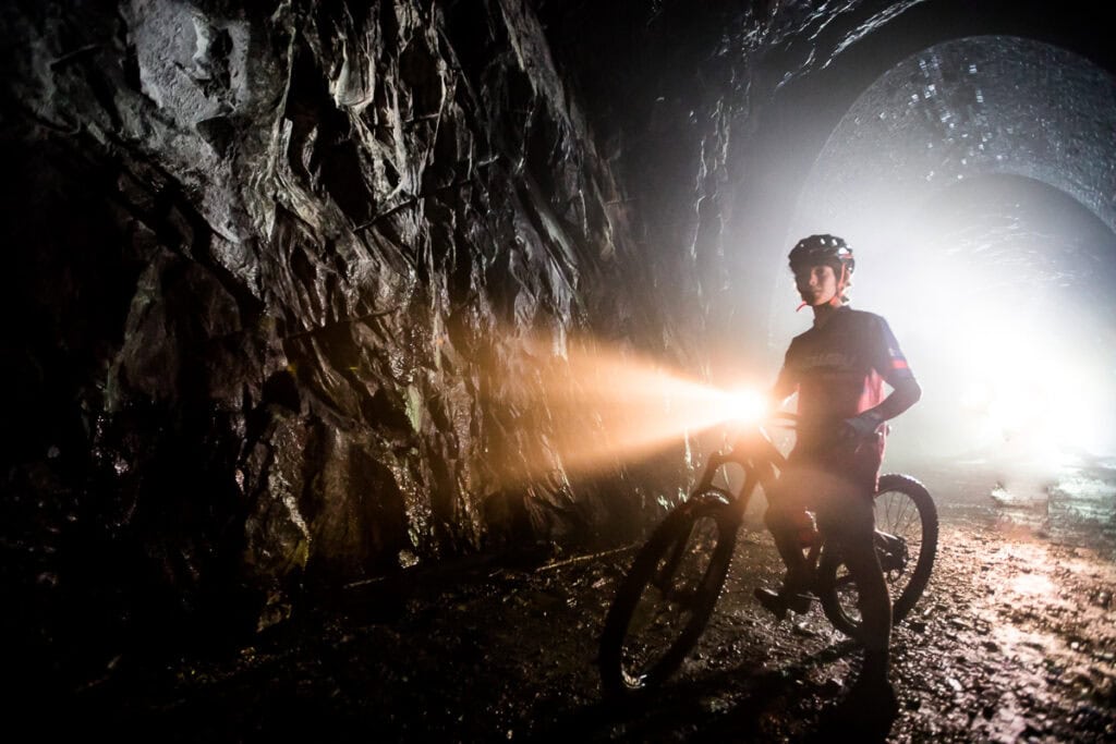 Cyclist with a bright headlamp riding through a dark stone railroad tunnel