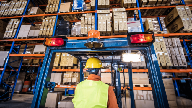forklift operator looking up at a tall rack of boxes
