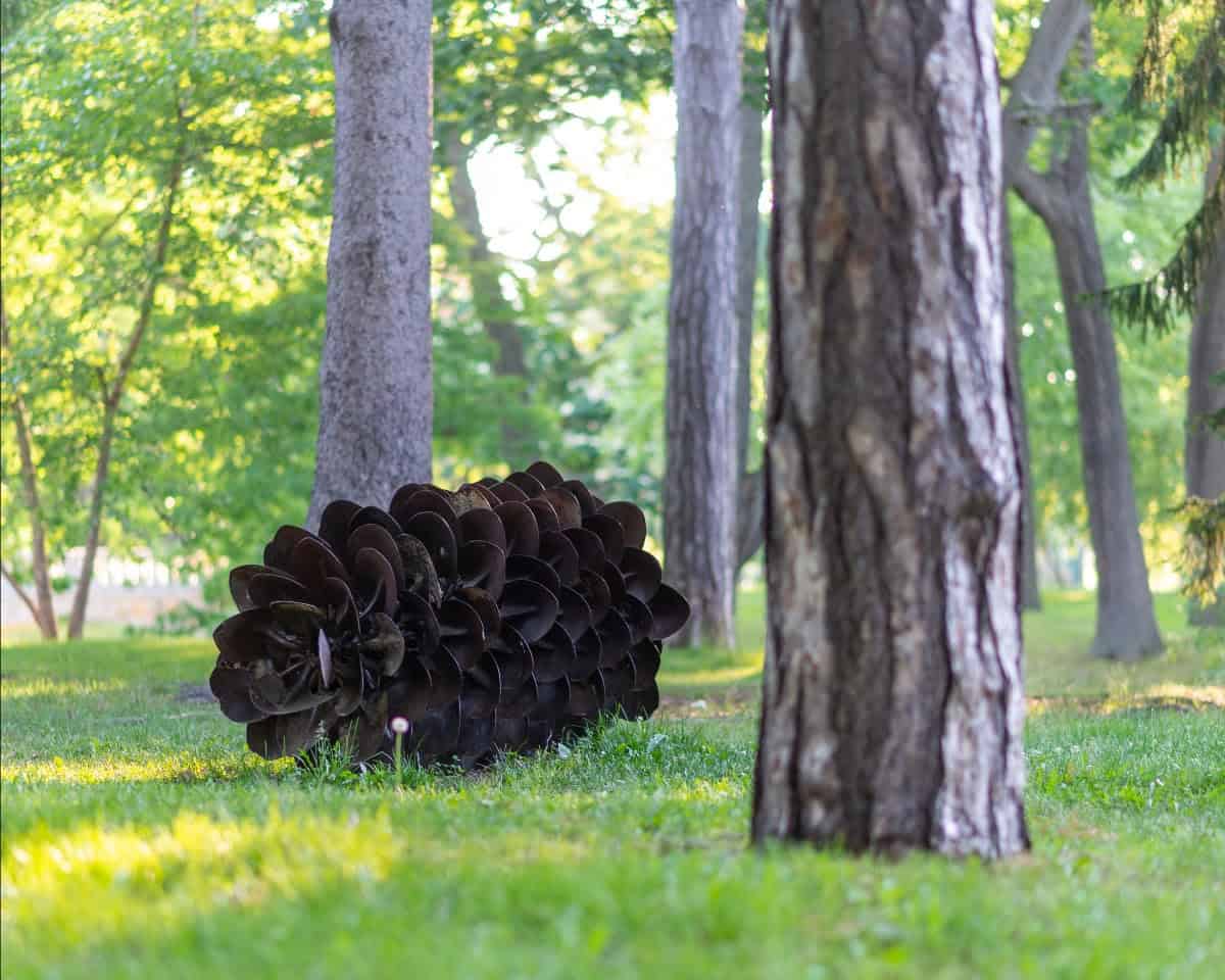 Artistic pinecone sculpture at dedication ceremony in a lush park setting.