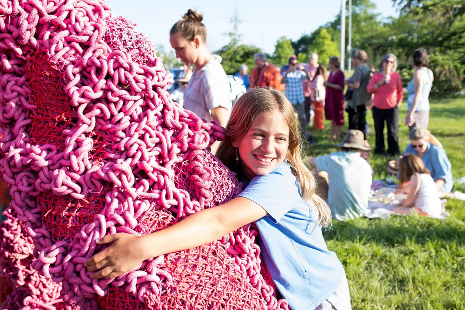 Girl hugging pink art sculpture at Think Pink art-making event outdoors.