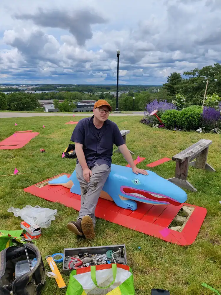Artist working on a large crocodile sculpture outdoors.