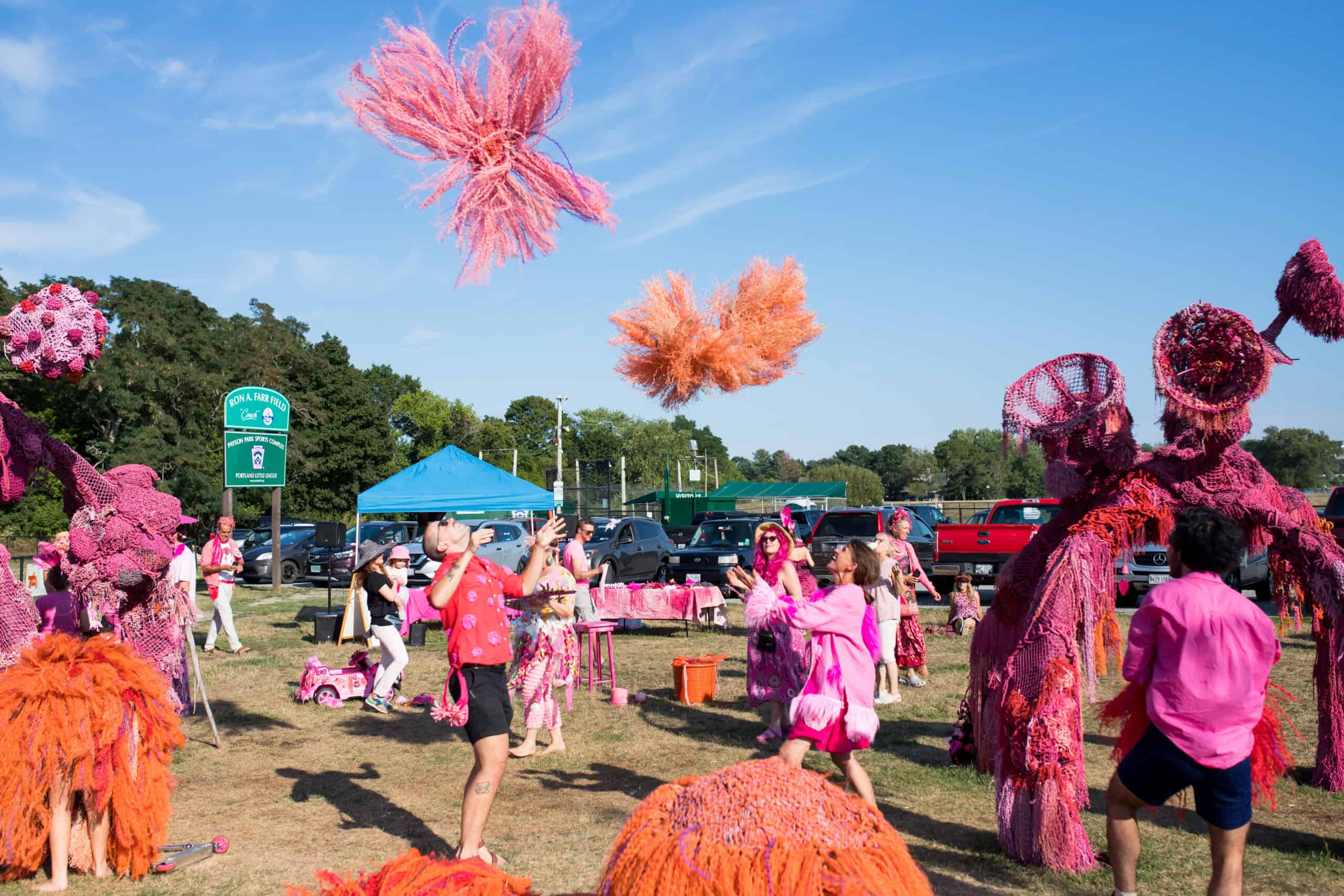 Vibrant pink and orange fiber art sculptures displayed outdoors during a community event.