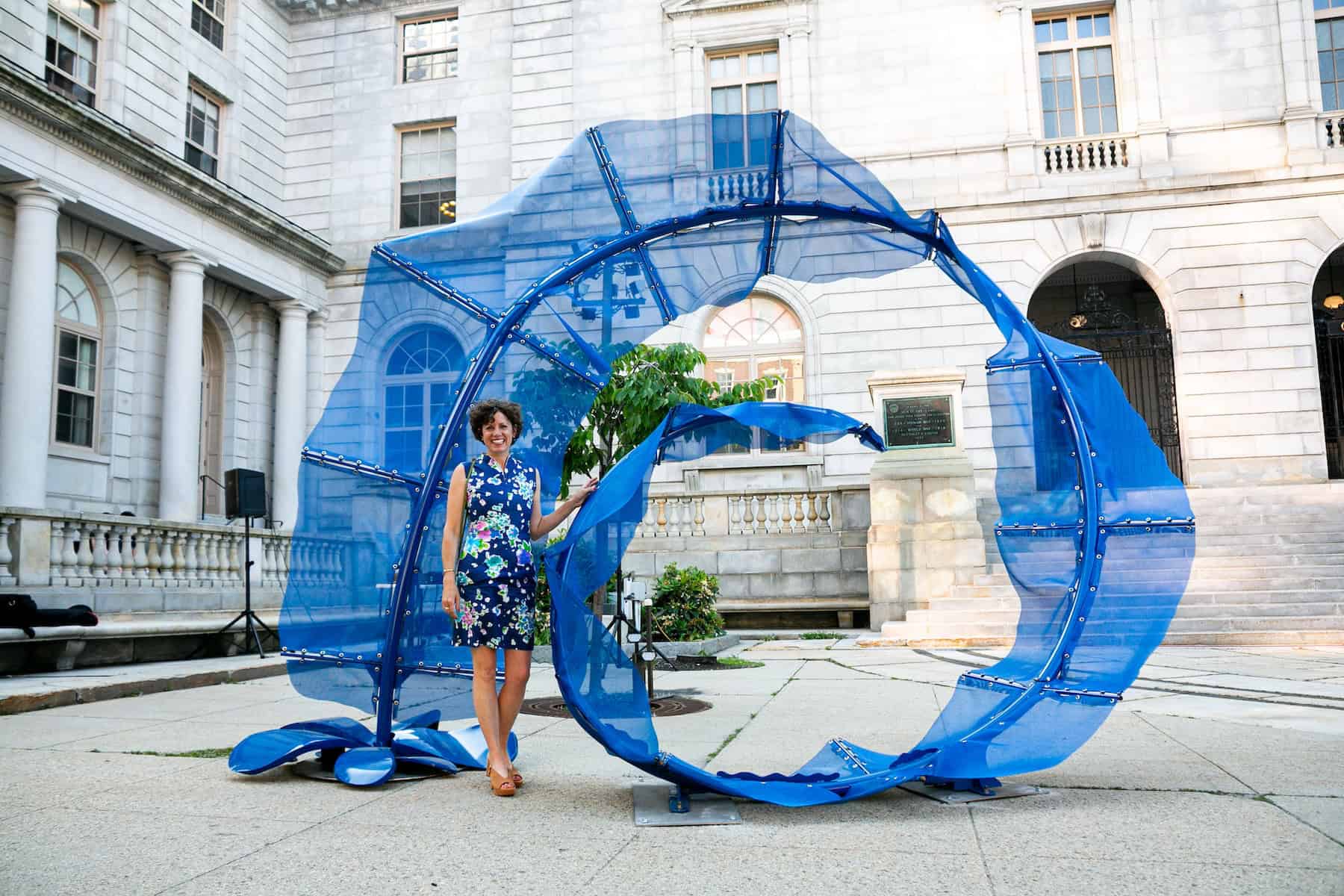 Contemporary blue fabric sculpture displayed outdoors in front of historic building.