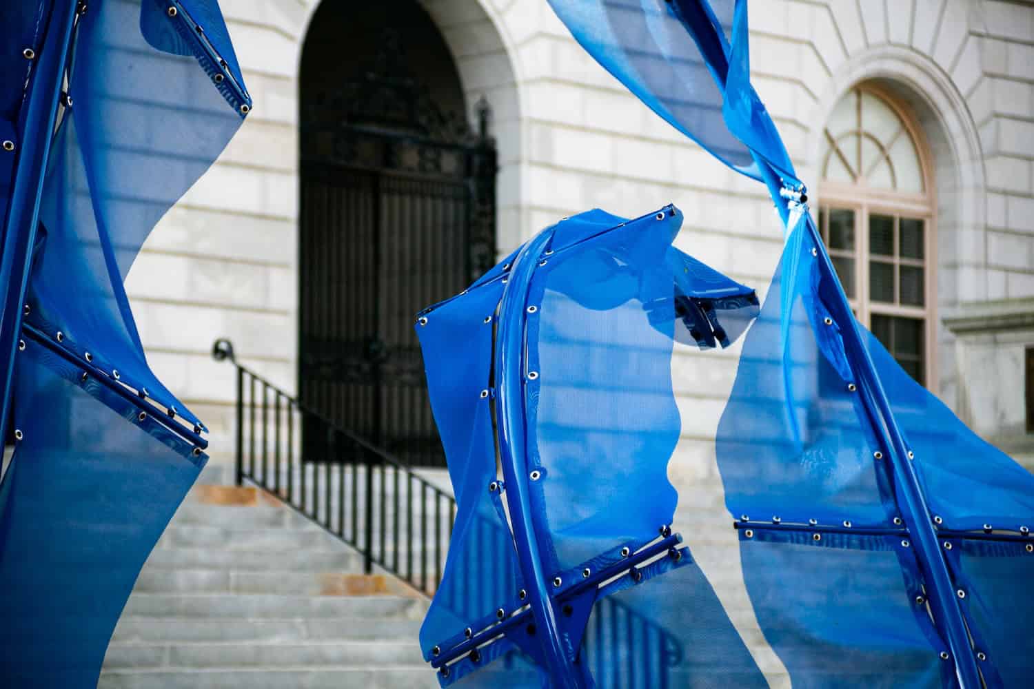 Blue fabric sculpture with flowing, dynamic shapes in front of a historic building.