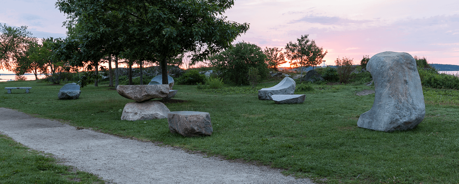 Stone sculpture park at sunset with large balanced rocks and lush greenery.