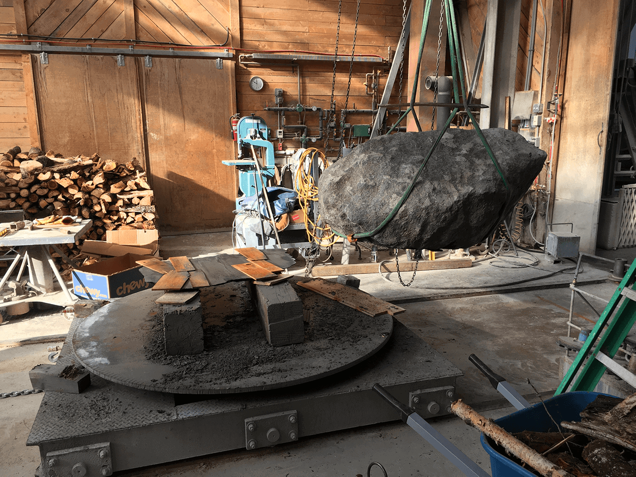 Industrial workshop with large stone being lifted by crane.