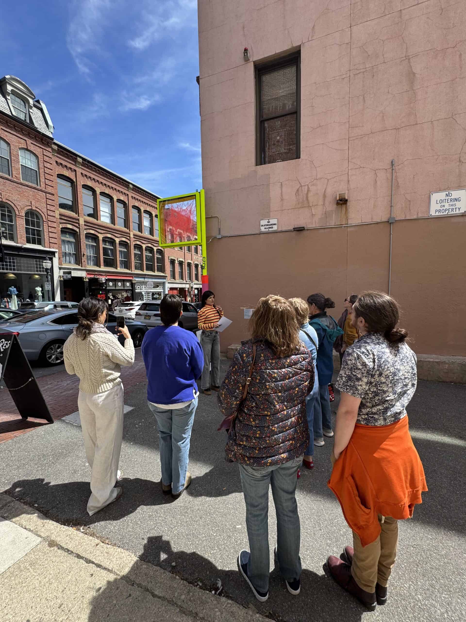 Group of diverse people waiting in line outside a building on a city street.