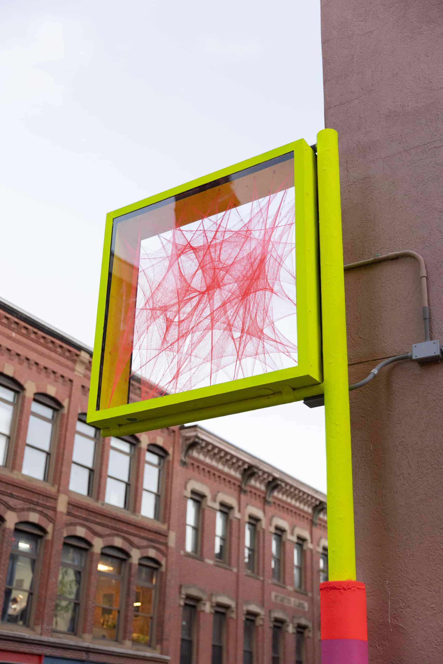 Colorful outdoor art installation with red string art in a yellow frame.