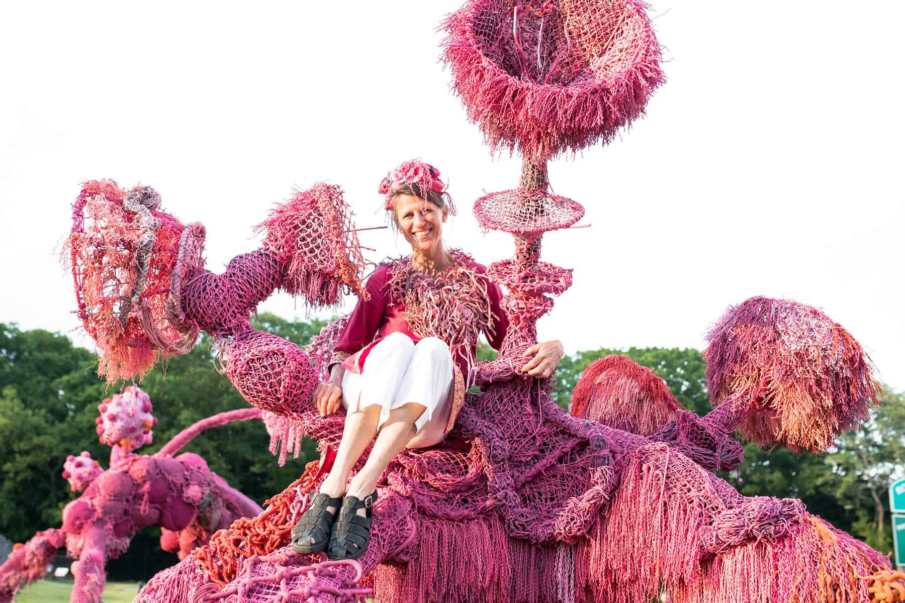 Colorful pink and purple floral sculpture with a smiling woman sitting on it.