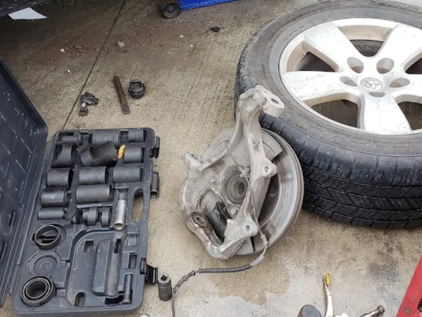 Car brake caliper and tire on garage floor at Texas Tire LLC.