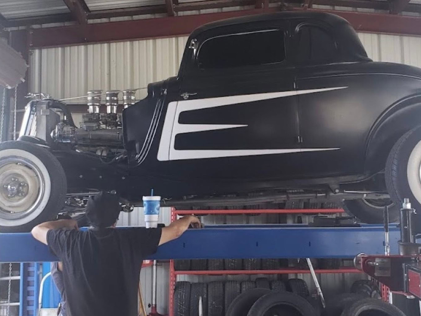 Vintage black car on lift at Texas Tire LLC auto shop.
