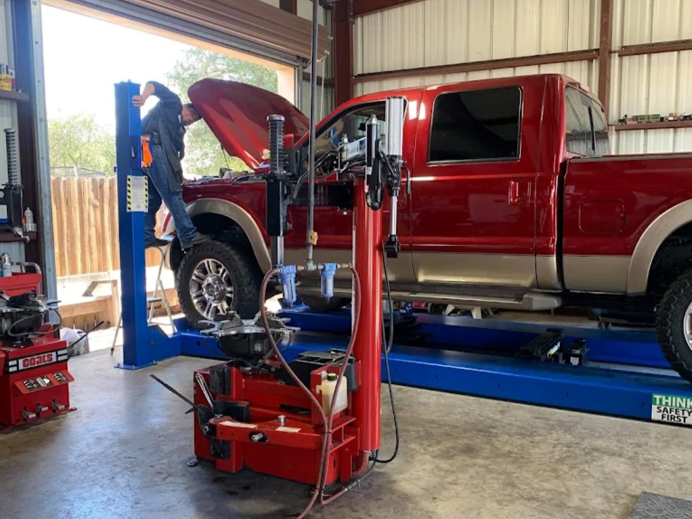 Red pickup truck on lift at Texas Automotive & Tire LLC workshop.