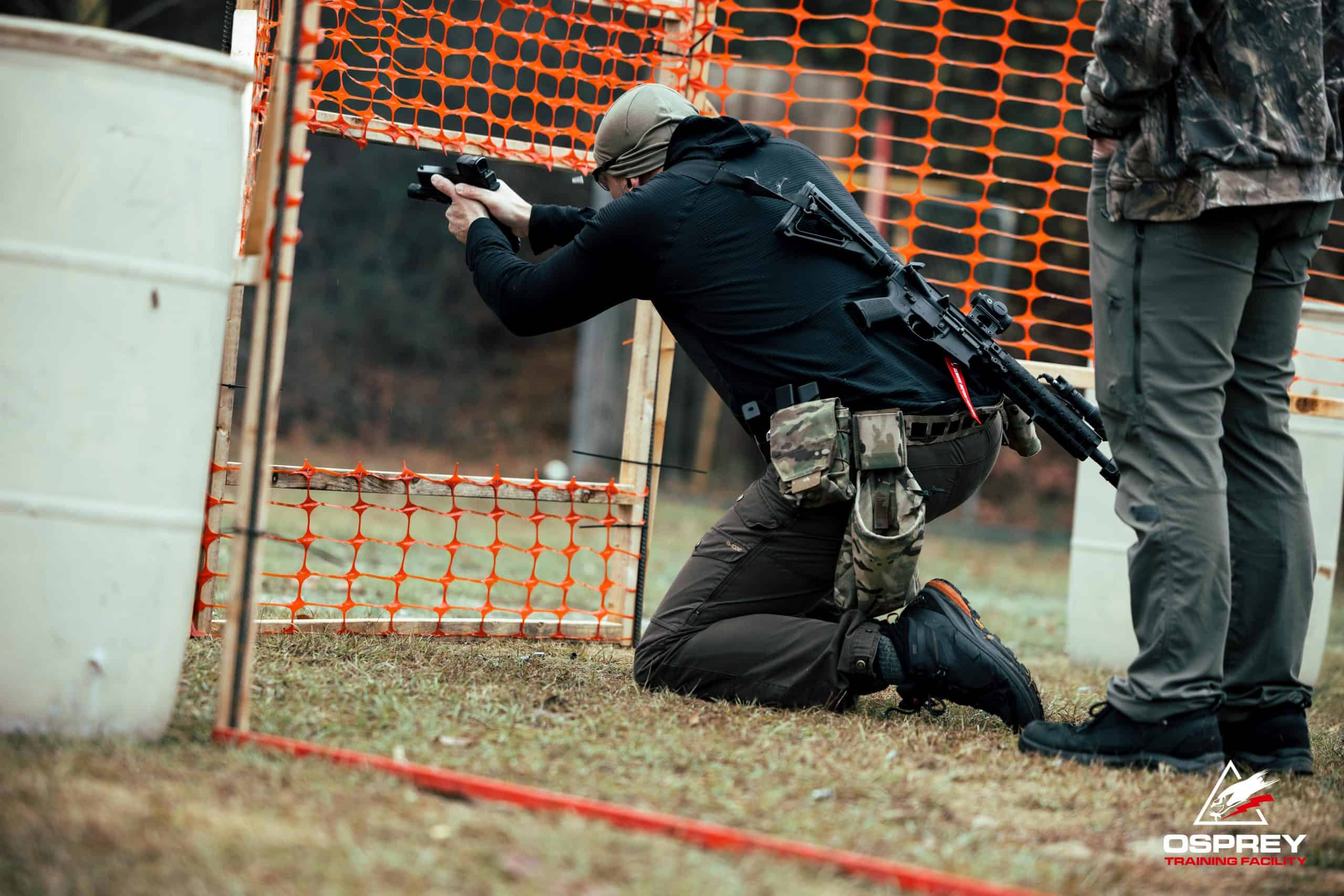 Competitor shooting pistol through an orange wall at a 2 Gun competition hosted by Osprey Training Facility