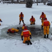 Rescue team performing ice rescue on frozen water in snowy outdoor setting.