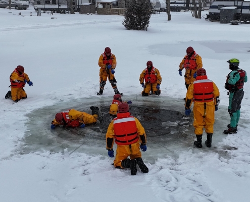 Rescue team performing ice rescue on frozen water in snowy outdoor setting.