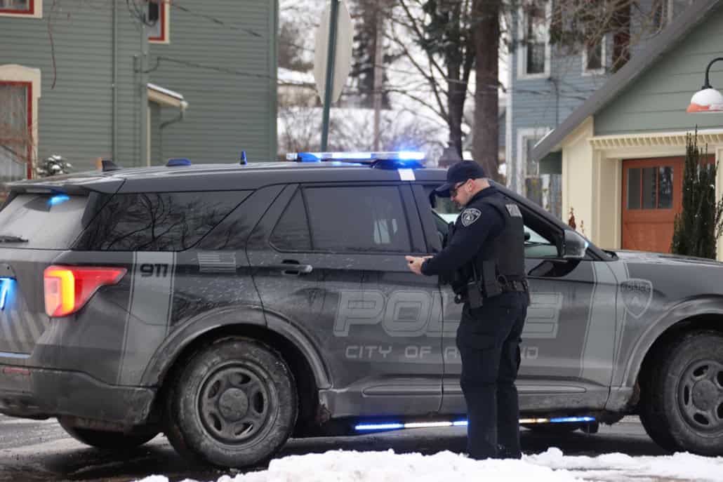Police officer using a mobile phone next to police vehicle on snowy street.