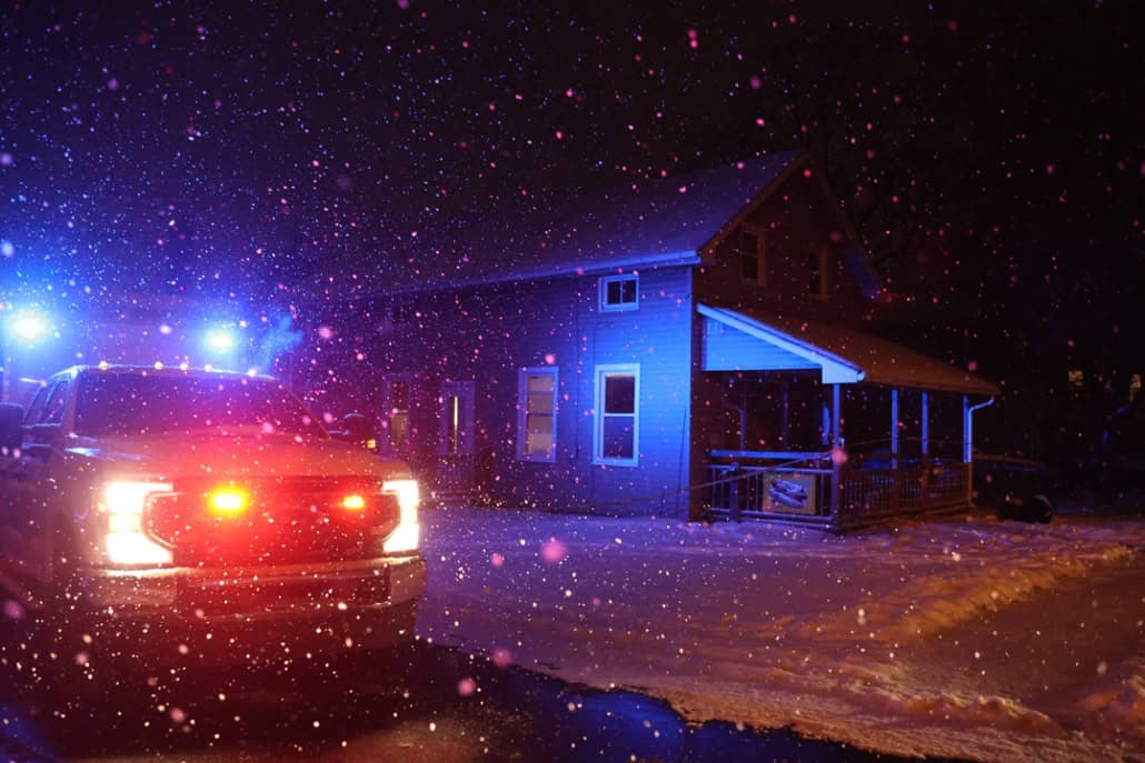 Snow falling at night with police vehicle lights illuminating a house in Fostoria, Ohio.