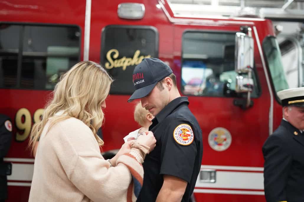 Emergency worker pinning badge on woman in front of fire truck.