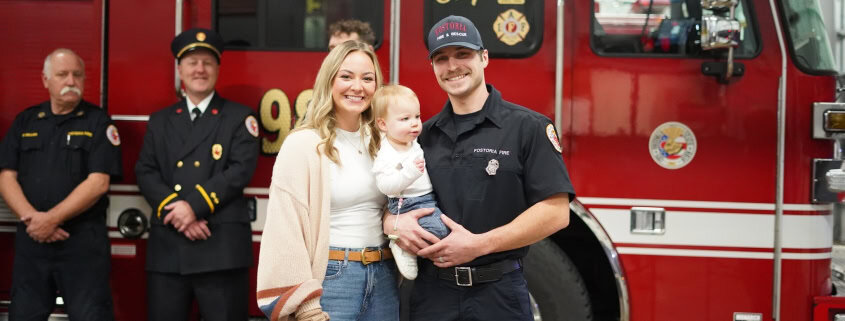 Rescue firefighter with family in front of fire truck at community event.