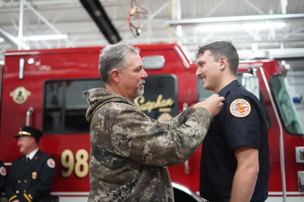 Father presenting fire department badge to young firefighter.