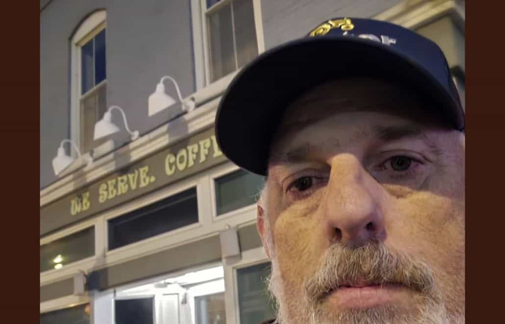 Close-up of a man wearing a police cap in front of a coffee shop, highlighting local news and community updates.