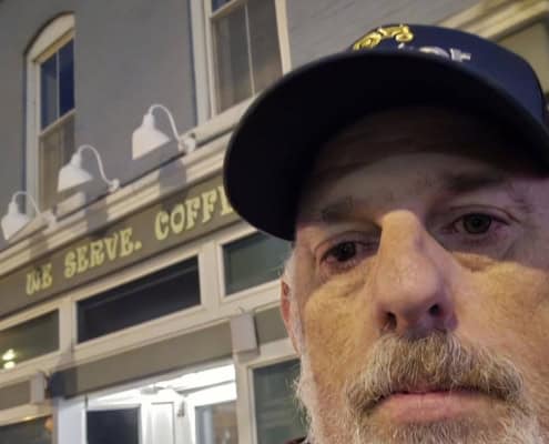 Close-up of a man wearing a police cap in front of a coffee shop, highlighting local news and community updates.