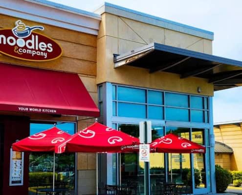 Noodles & Company restaurant exterior with outdoor seating and branded red umbrellas.