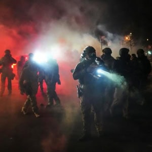 Police officers in tactical gear during night operation with smoke and bright lights in Fostoria, Ohio.