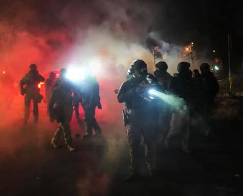 Police officers in tactical gear during night operation with smoke and bright lights in Fostoria, Ohio.