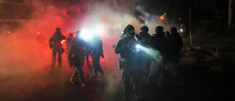 Police officers in tactical gear during night operation with smoke and bright lights in Fostoria, Ohio.
